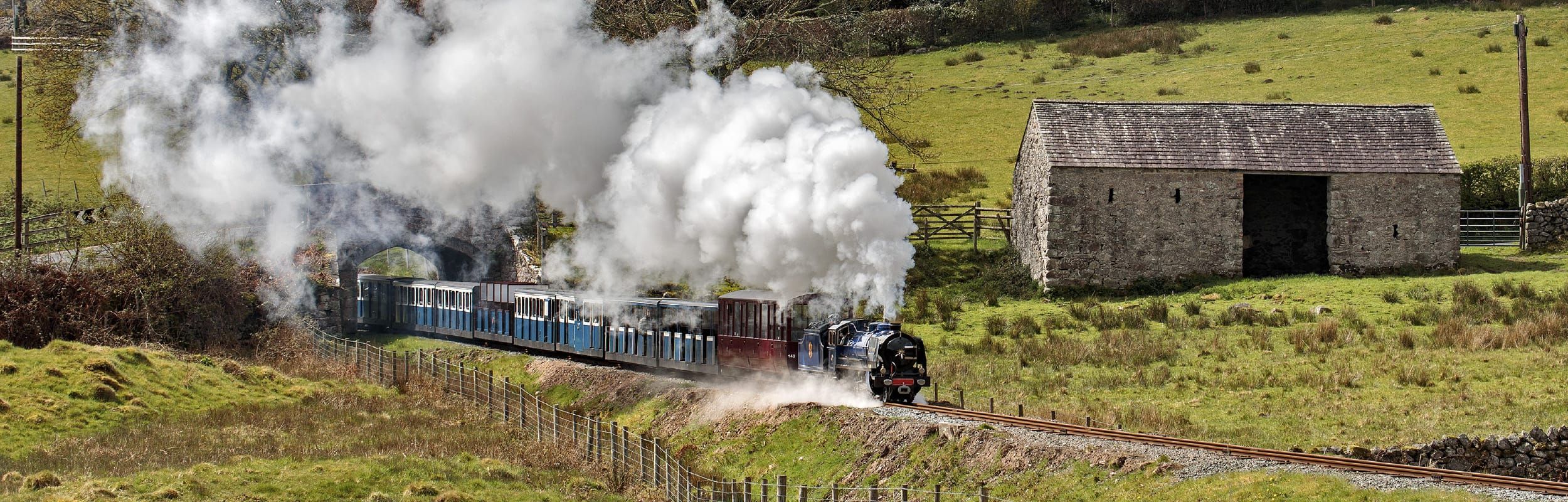 Whillan Beck, a heritage locomotive at the Ravenglass and Eskdale railway hauling a train through a cloud of steam