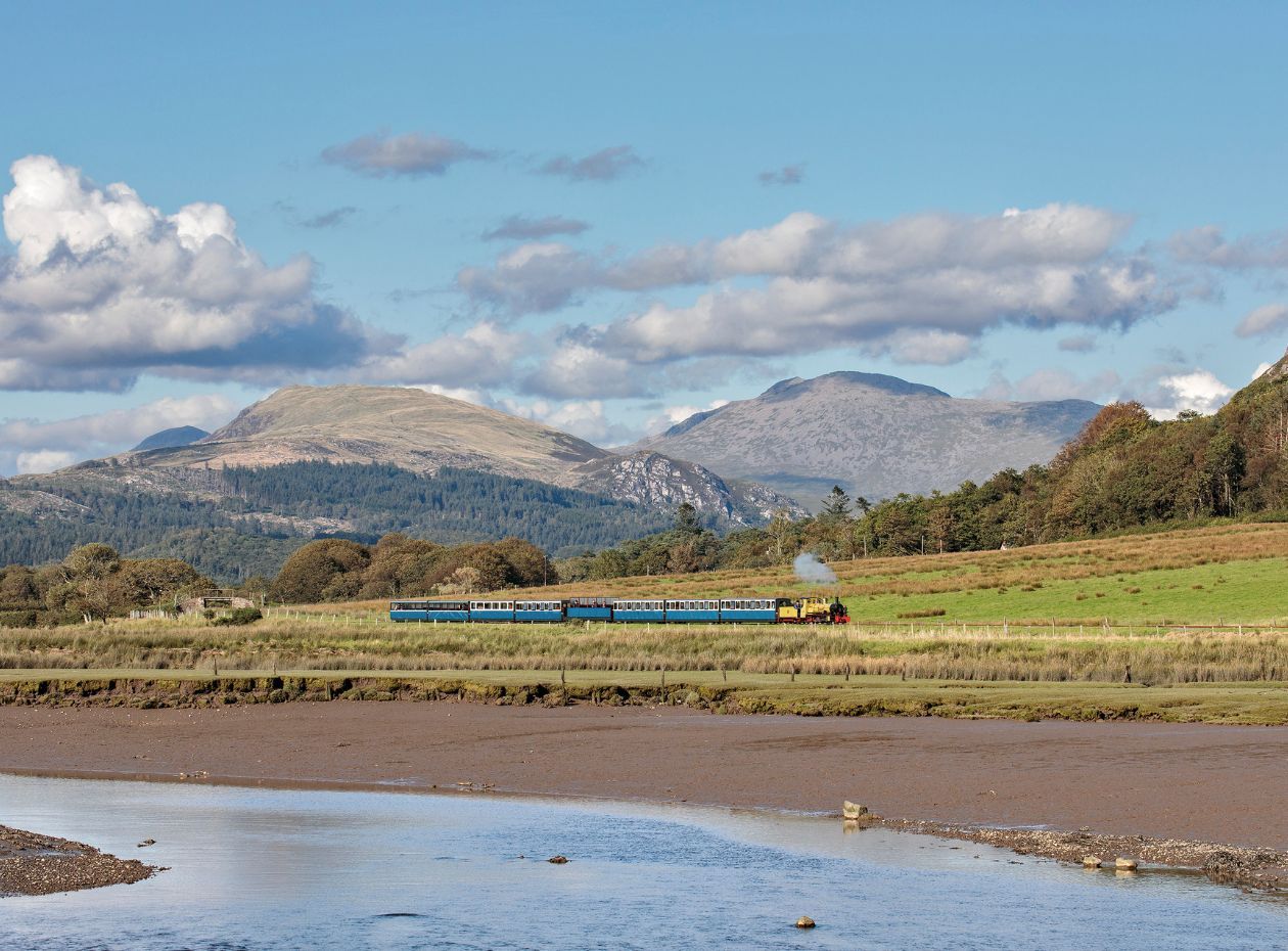 A steam train travelling on the Ravenglass and Eskdale Railway with Lake District mountains in the background